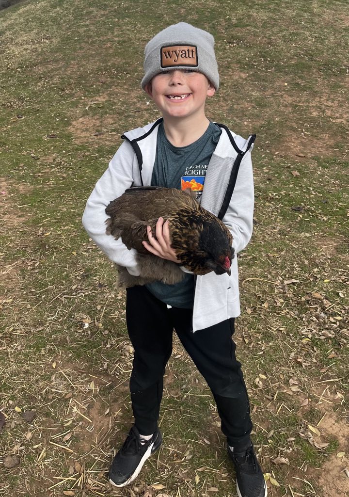 A grinning student in a gray beanie and white jacket holding a big brown and black hen