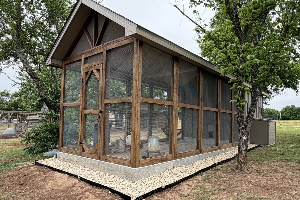 The new chicken coop on the Terra Verde campus: a wood-framed, screened coop with a peaked roof on a concrete base, edged with white rock